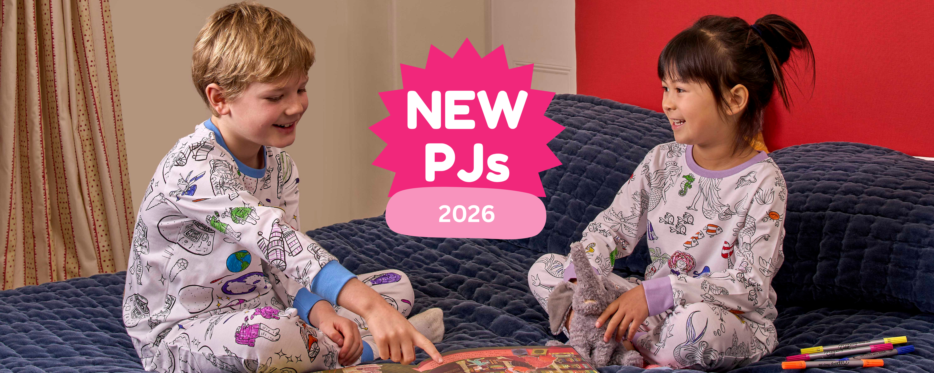 boy wearing space pyjamas sat on bed reading with girl in mermaid pyjamas